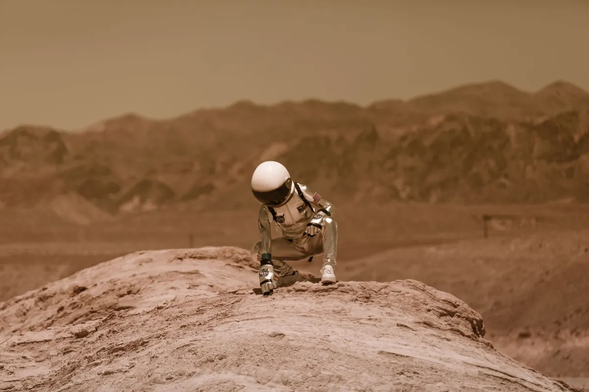 An astronaut in a space suit exploring a Mars-like desert environment, crouching on a rocky surface.