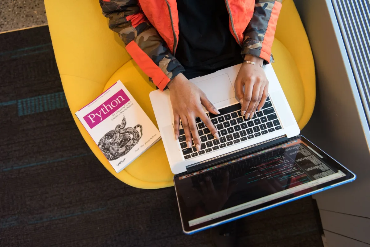 Developer typing Python code on a laptop beside a Python book