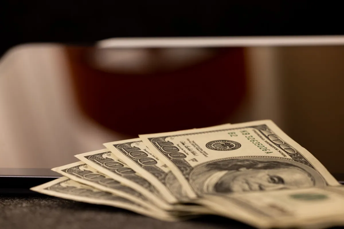 Close-up image of multiple dollar bills placed beside a laptop, symbolizing finance and digital economy.