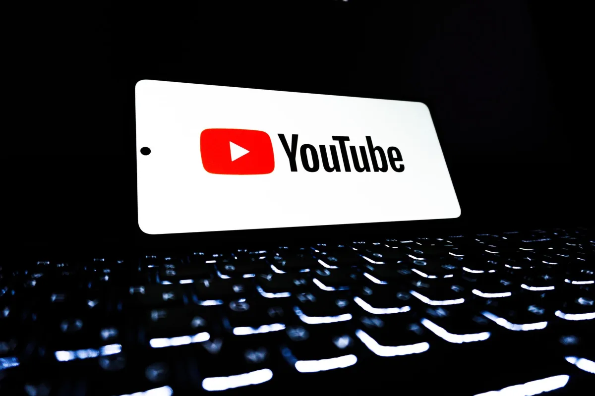 A smartphone displaying the YouTube app next to a laptop keyboard, illustrating digital video content.