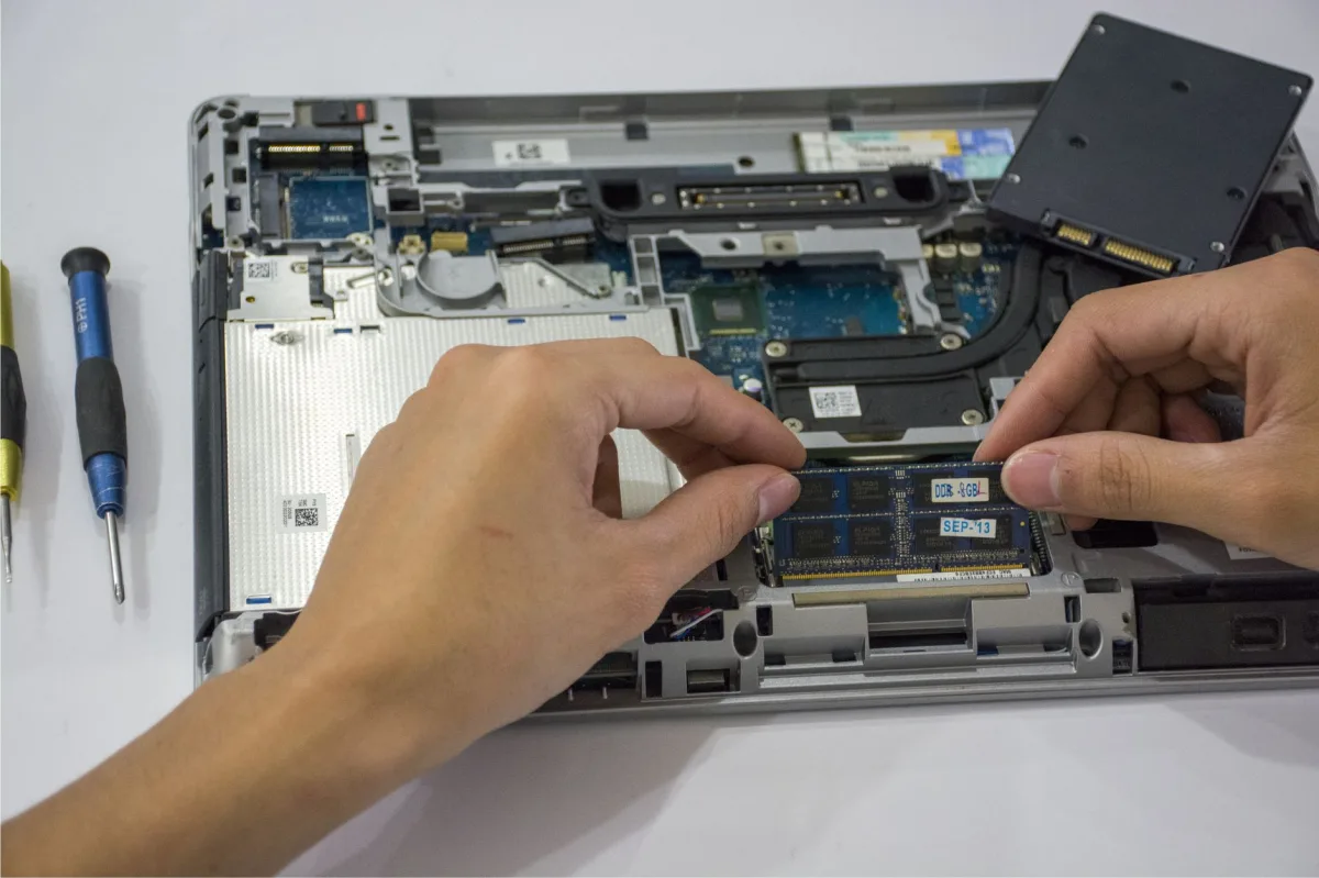 Technician assembling a laptop's internal components using tools.